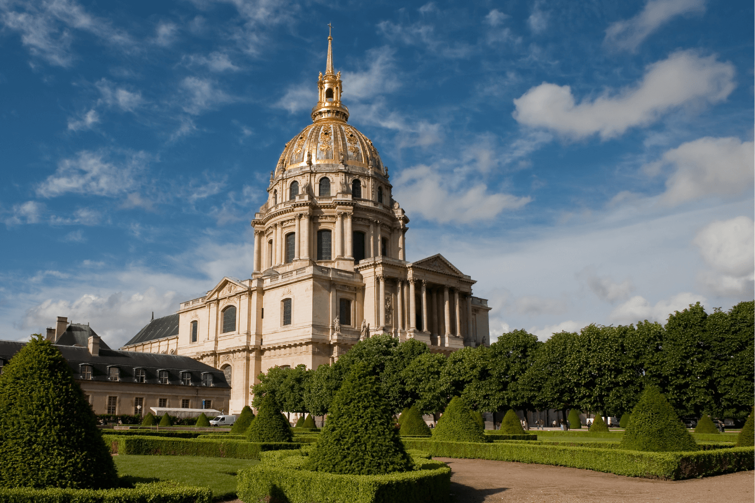 The Hôtel des Invalides in Paris's 7th arrondissement, featuring its iconic golden dome, stands under a bright blue sky with scattered clouds. 