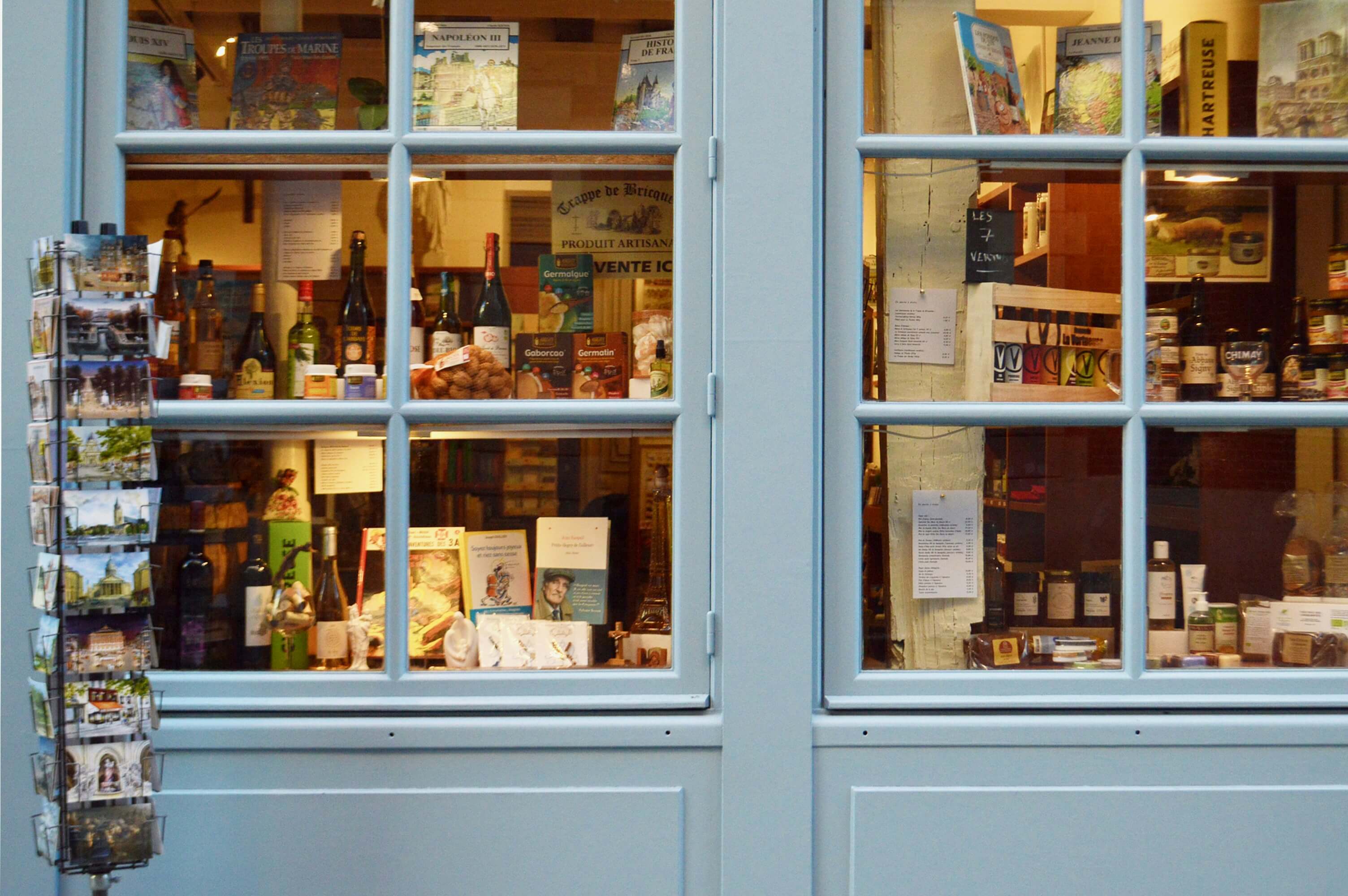 La vitrine d’une librairie parisienne, présentant une sélection de livres, de cartes postales et d’objets artisanaux, reflétant le charme chaleureux et culturel de la boutique.