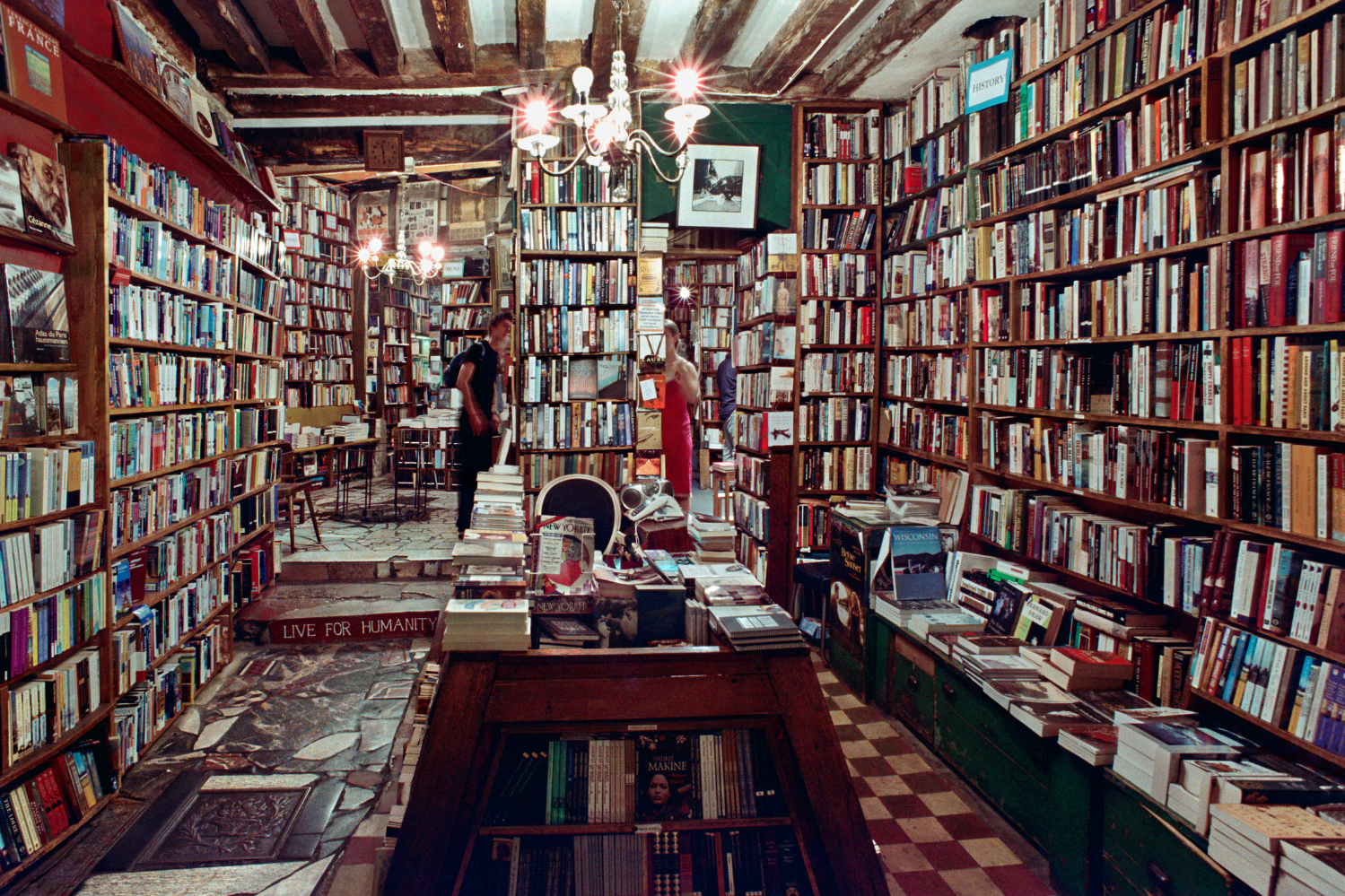 Intérieur de la célèbre librairie Shakespeare and Company à Paris, avec des murs recouverts de livres, des poutres en bois, des coins lecture chaleureux et une ambiance vintage.