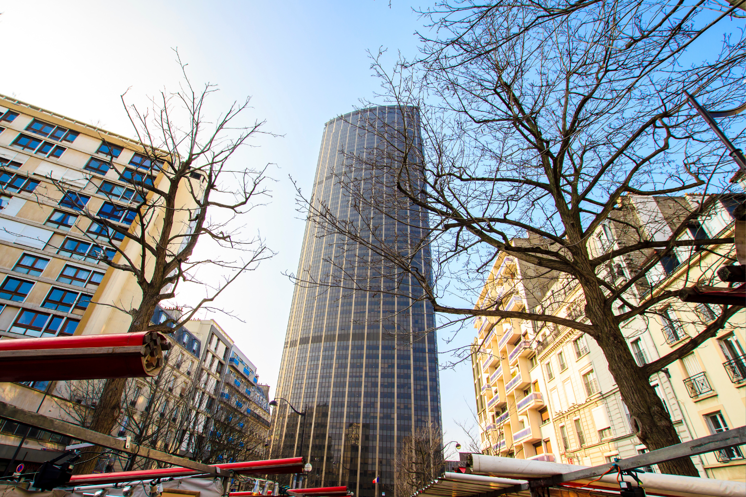 La Tour Montparnasse à Paris, un gratte-ciel moderne entouré d’immeubles résidentiels et d’arbres dénudés, vue depuis le niveau de la rue par une journée dégagée.