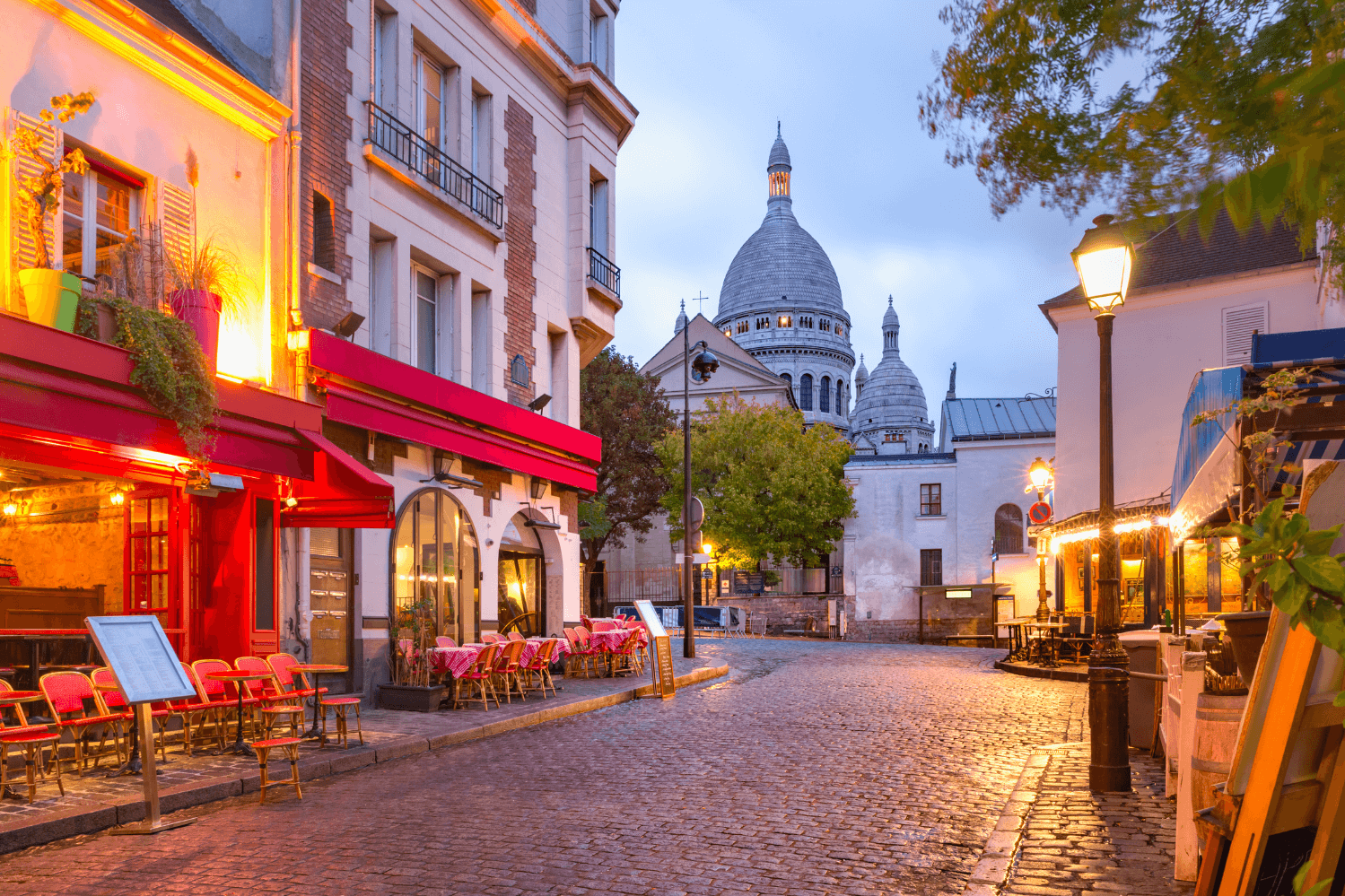 Charming cobblestone streets of Montmartre at dusk, featuring cozy Parisian cafes and the iconic Sacré-Cœur Basilica in the background, a must-visit destination in Paris.