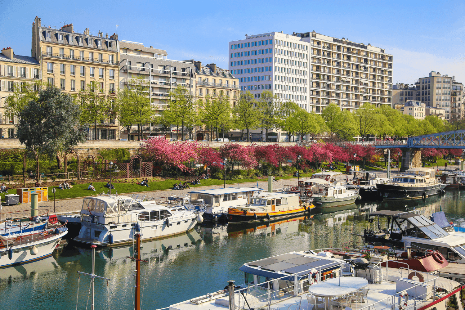 Canal Saint-Martin in Paris, showcasing picturesque houseboats, blooming cherry trees, and vibrant urban life