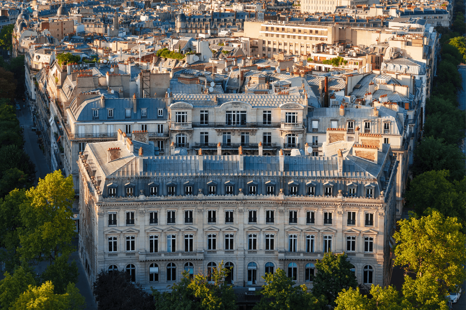 View of classic French architecture with elegant buildings, slate rooftops, and tree-lined streets in the heart of Paris, showcasing the charm of Parisian real estate.