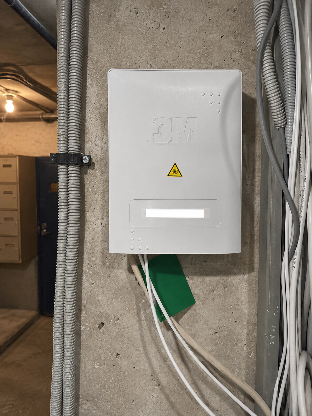 Fiber optic distribution box in the building’s technical basement area, with cables and conduits mounted on a concrete wall.